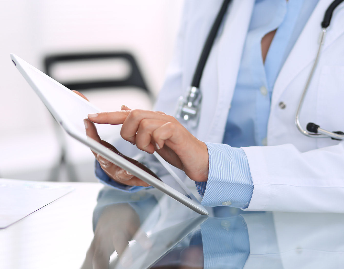 A doctor in white coat examines patient data on a tablet, showcasing the use of technology in healthcare settings.